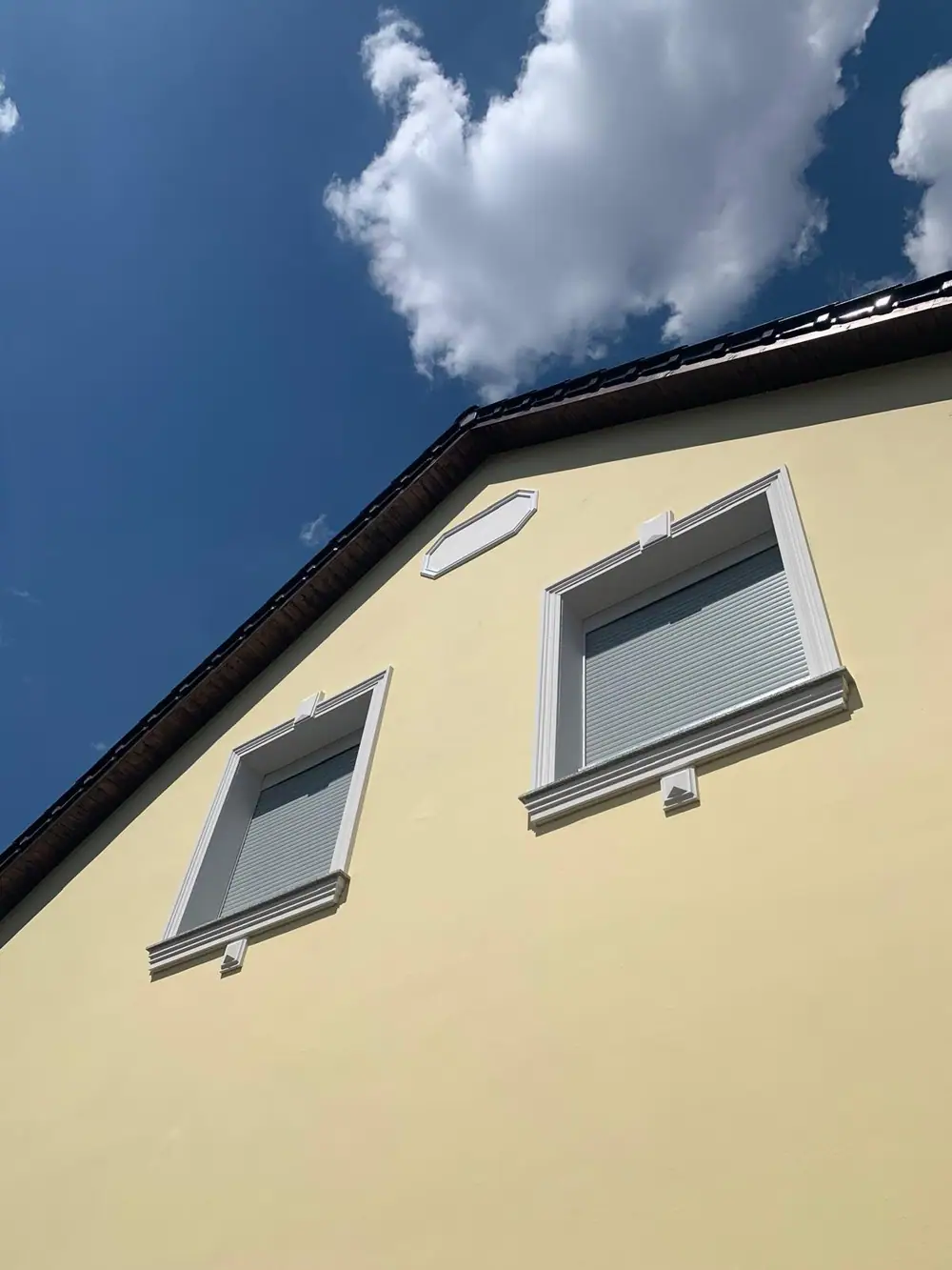 Gelber Giebel mit weißen Fensterfaschen vor blauem Himmel
